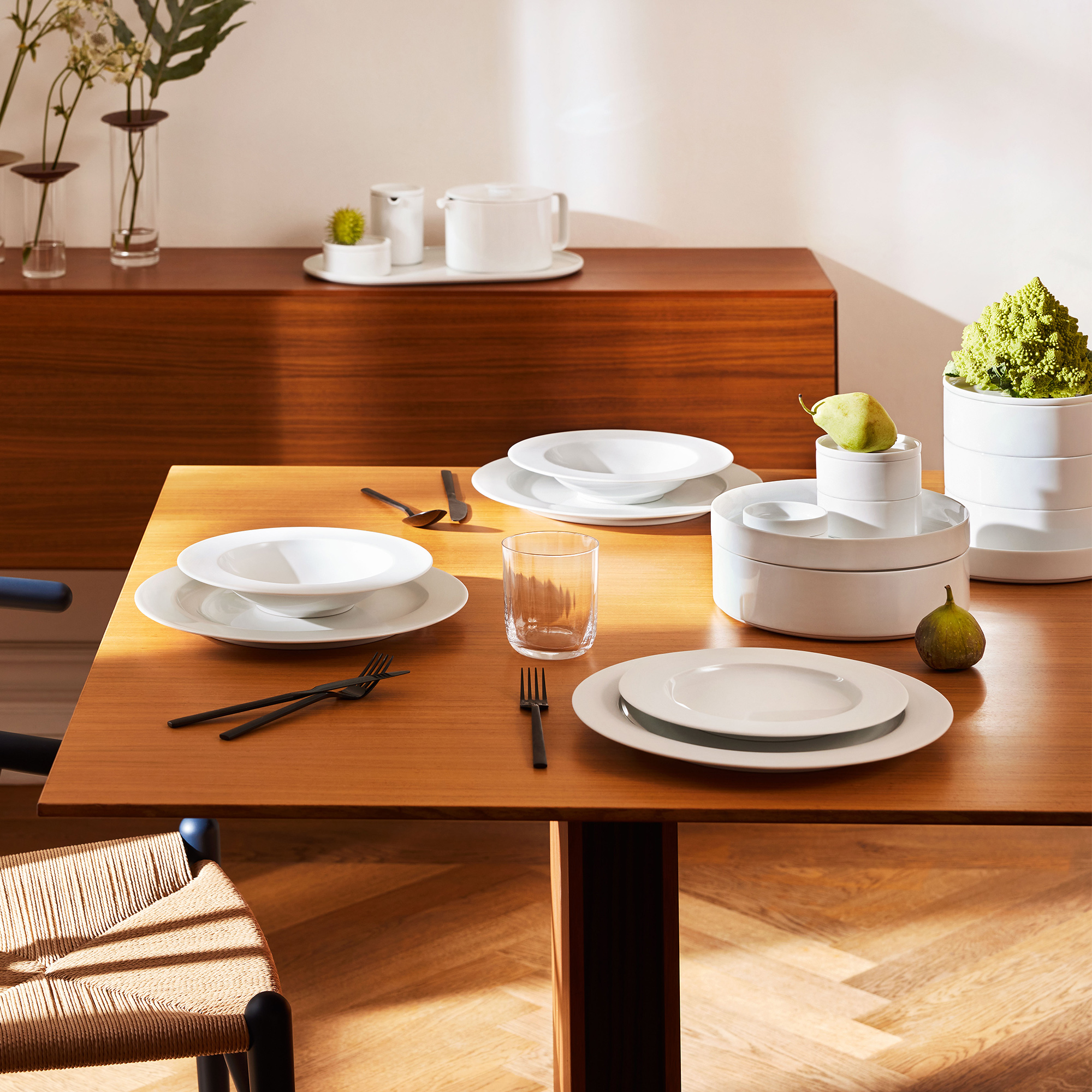 Gedeckter Holztisch mit weißem Porzellangeschirr, Figürchen und Glas. Fürstenberg Porzellan.