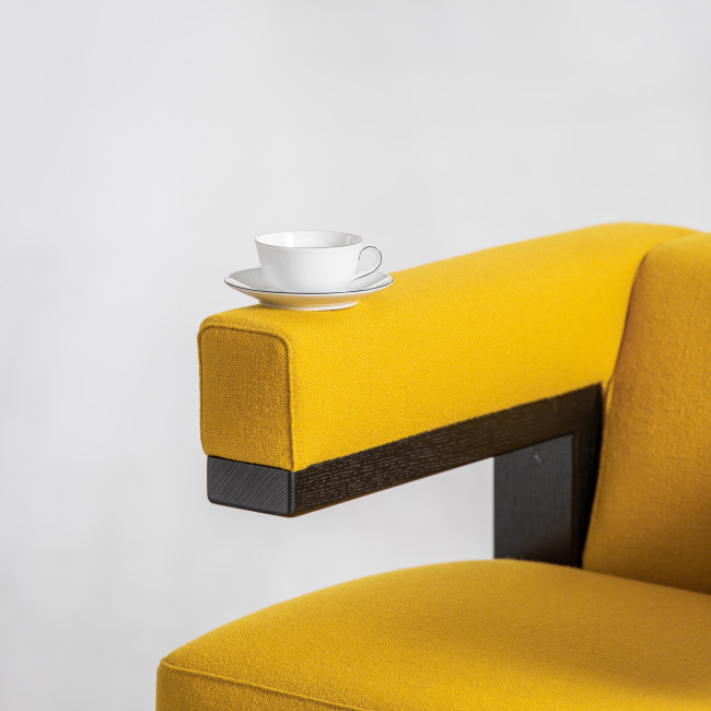 Weiße Tasse auf gelbem Sofalehnenrand, minimalistisch angeordnet. Fürstenberg Porzellan.
