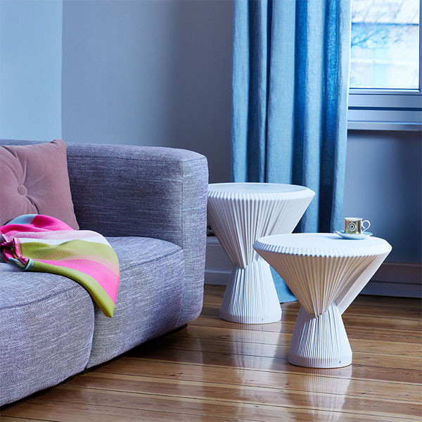 Weiße Porzellan-Hocker neben grauem Sofa, Tasse auf Hocker, bunte Decke. Fürstenberg Porzellan.