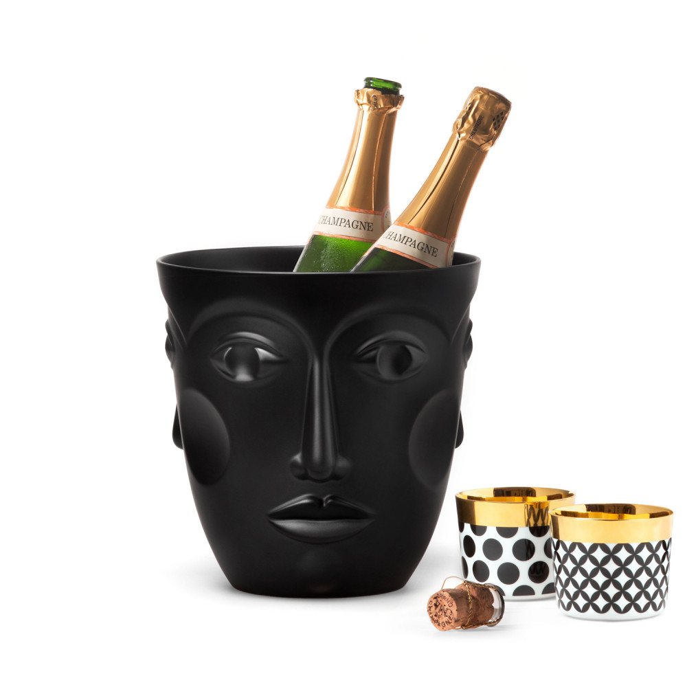 Schwarzer Eiskübel in Gesichtsform hält Champagnerflaschen, neben goldverzierten Tassen. Fürstenberg Porzellan.