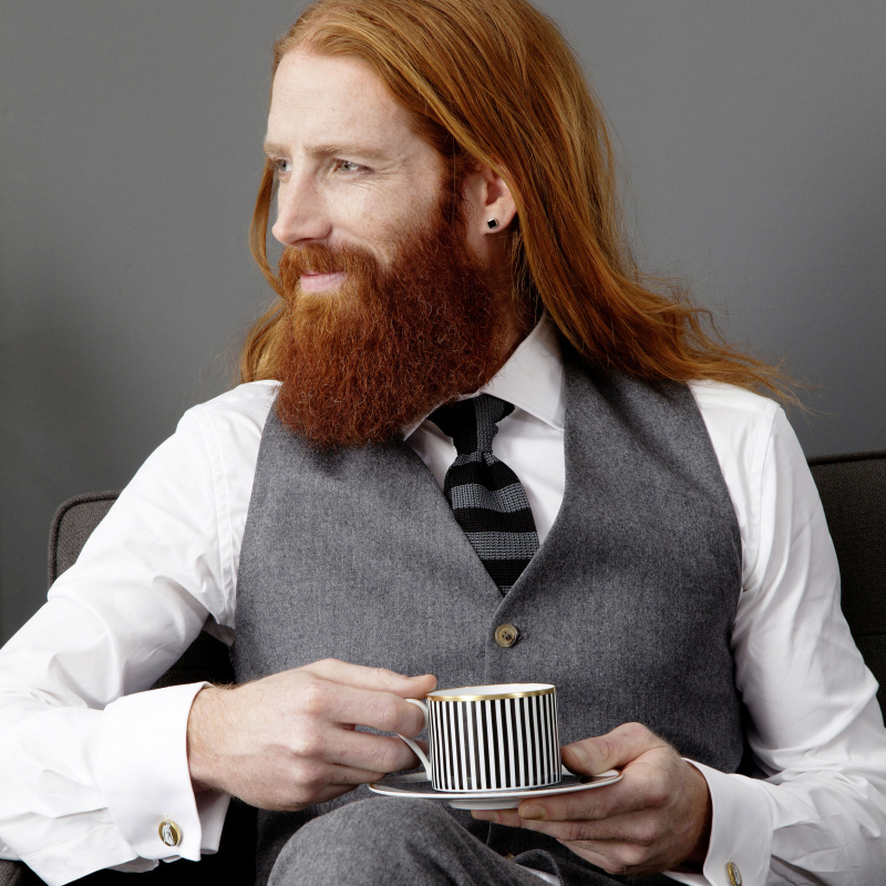 img2_ob20065_5705_kaffeeobertasse Mann hält gestreifte Tasse sitzend auf Sofa, schaut nach links. Fürstenberg Porzellan.