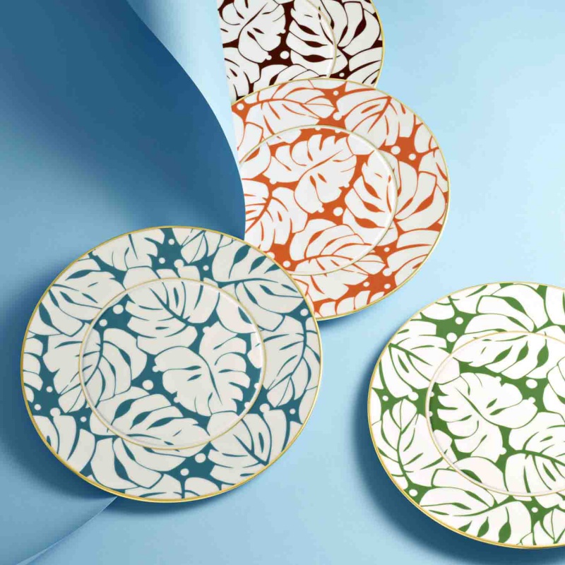img4_fl20143270023_platzteller Vier Porzellanteller mit Blattmuster in verschiedenen Farben liegen auf blauem Hintergrund. Fürstenberg Porzellan.