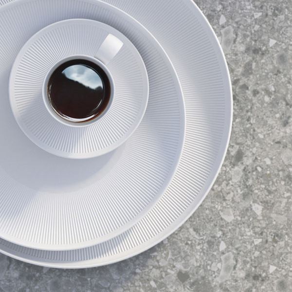 Weiße geriffelte Teetasse und Teller auf grauem Steinuntergrund, Teetasse gefüllt. Fürstenberg Porzellan.