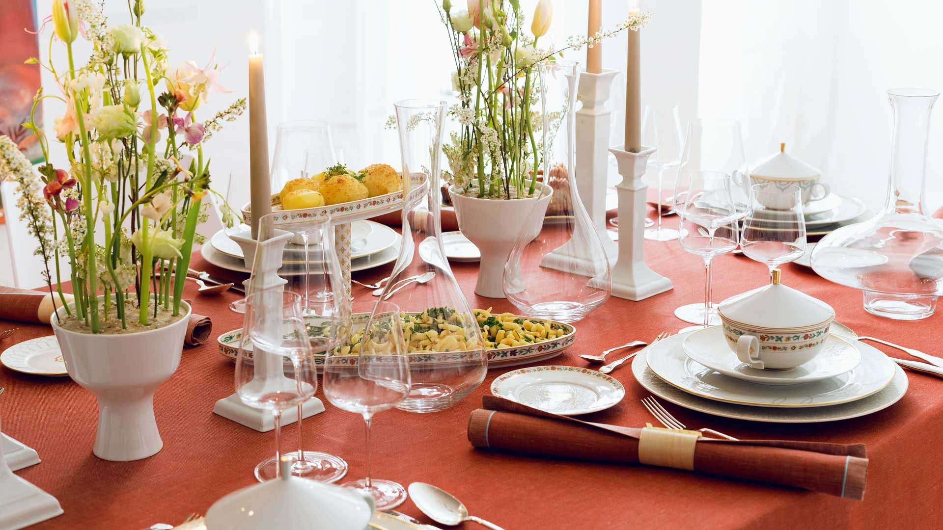 Table culture Elegante Tischdekoration mit weißem Porzellangeschirr und Blumen auf roter Tischdecke. Fürstenberg Porzellan.