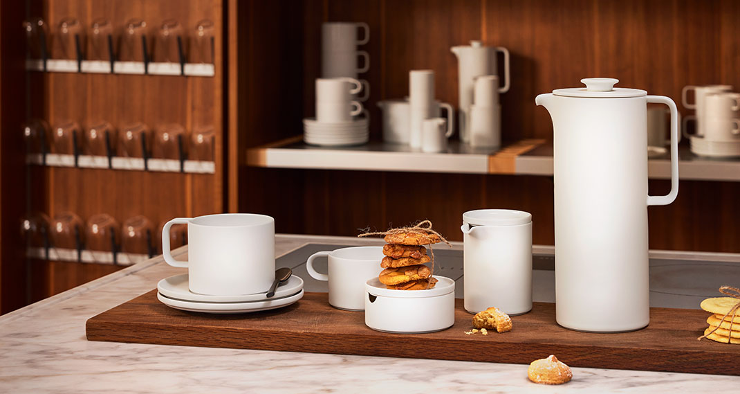 Weiße Porzellantassen, Kanne und Plätzchen auf Holztisch in modernem Regal. Fürstenberg Porzellan.