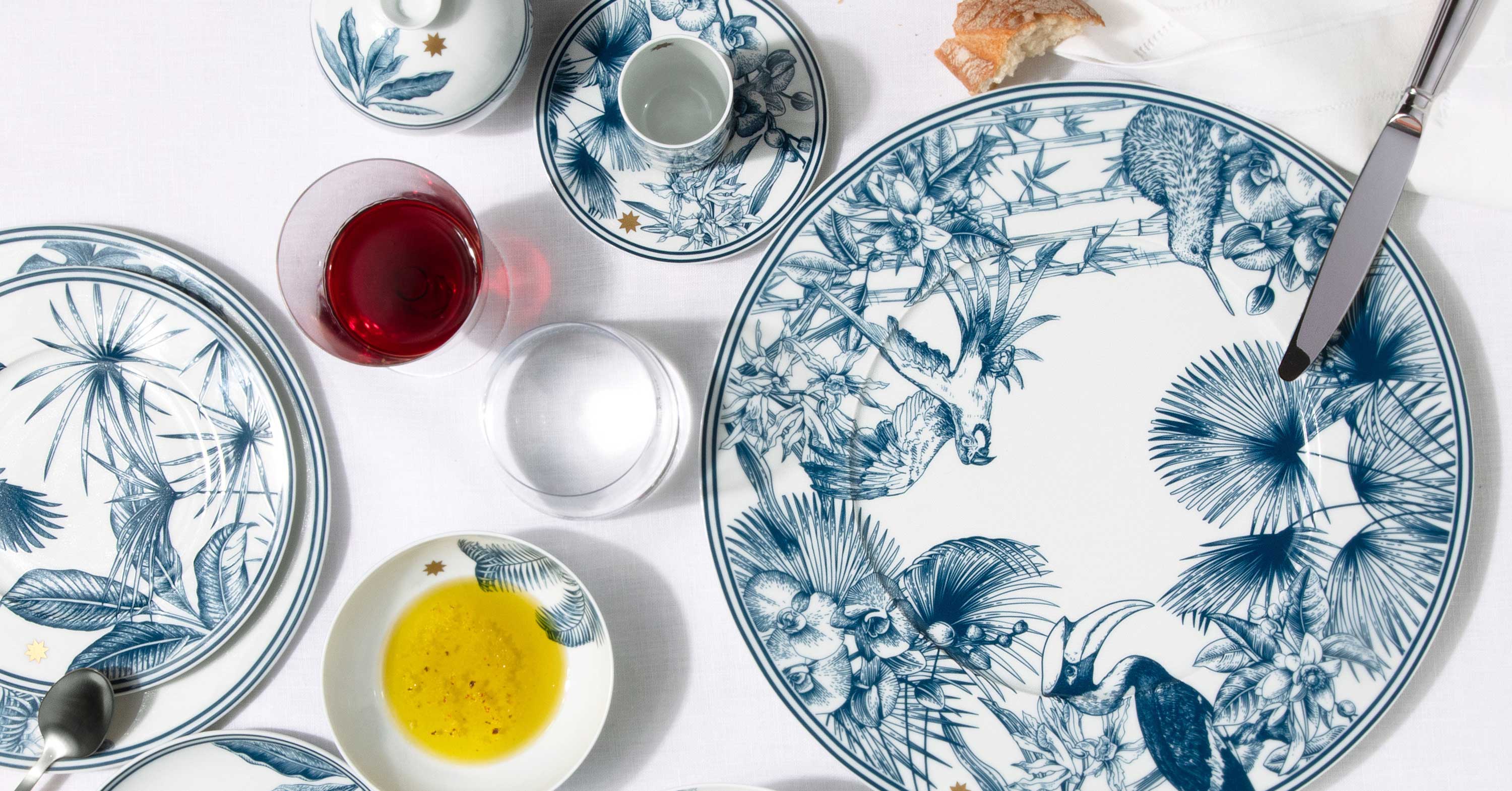 Teller mit blauen tropischen Motiven, aufgedecktem Besteck und Weinglas auf weißer Tischdecke. Fürstenberg Porzellan.