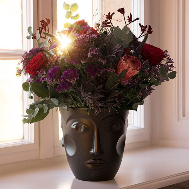 img3_ck1857256102_sektkuehler_faces__satin_black Schwarze Gesichtsvase hält bunte Blumen vor einem sonnigen Fenster. Fürstenberg Porzellan.