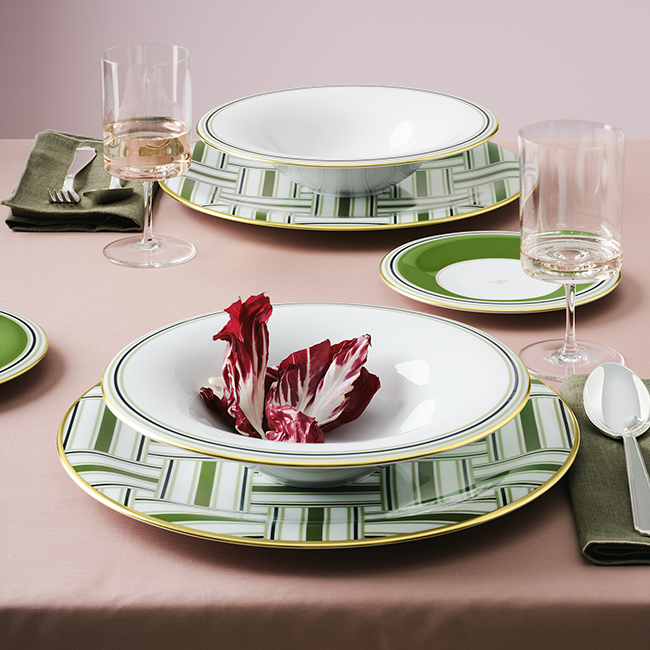 Porzellangeschirr zeigt grünes Muster, Wein-Gläser und Radicchio auf rosa Tischdecke. Fürstenberg Porzellan.