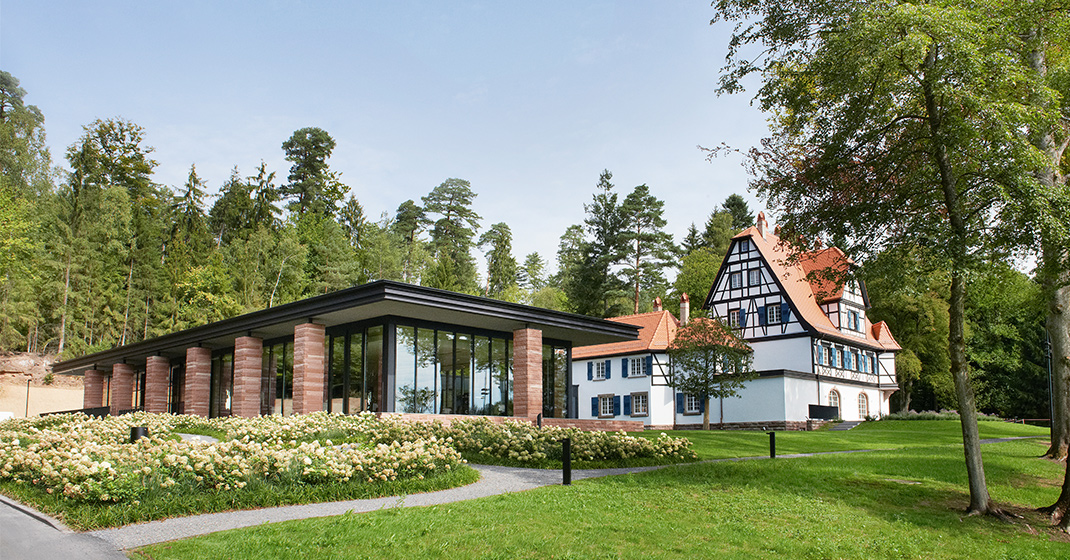 Modernes Gebäude, Fachwerkhaus, grüne Umgebung, Bäume, blauer Himmel. Fürstenberg Porzellan.