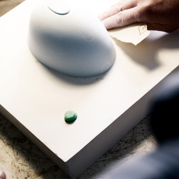 Hand schleift grauen Porzellanhut auf weißem Tisch mit grünem Knopf. Fürstenberg Porzellan.