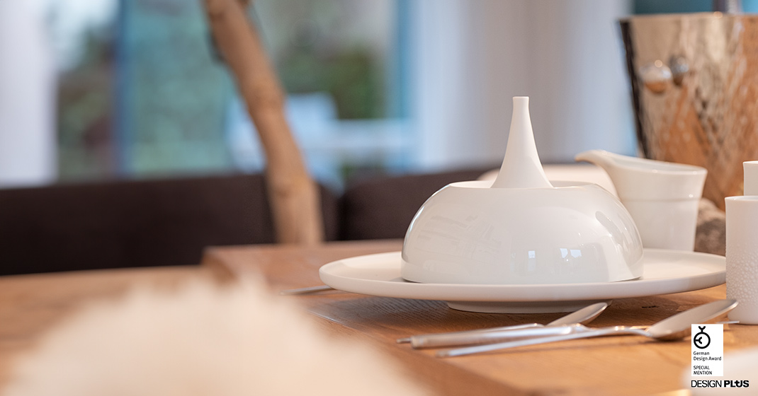 Weiße Porzellanschale mit Haube steht auf gedecktem Holztisch, Design Plus Auszeichnung. Fürstenberg Porzellan.