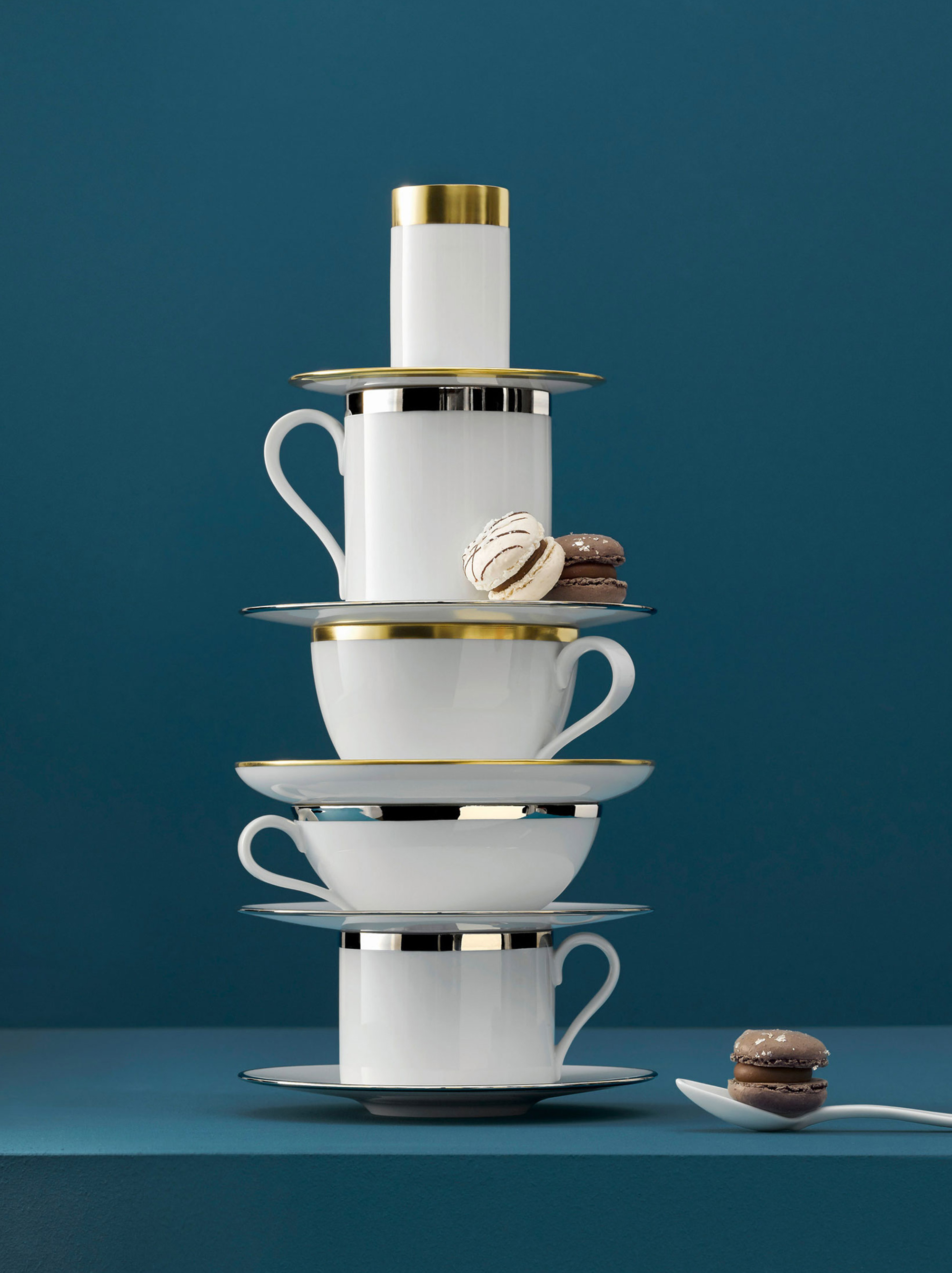 Gestapelte Tassen mit goldenen Rändern, Teller und Macarons vor blauem Hintergrund. Fürstenberg Porzellan.