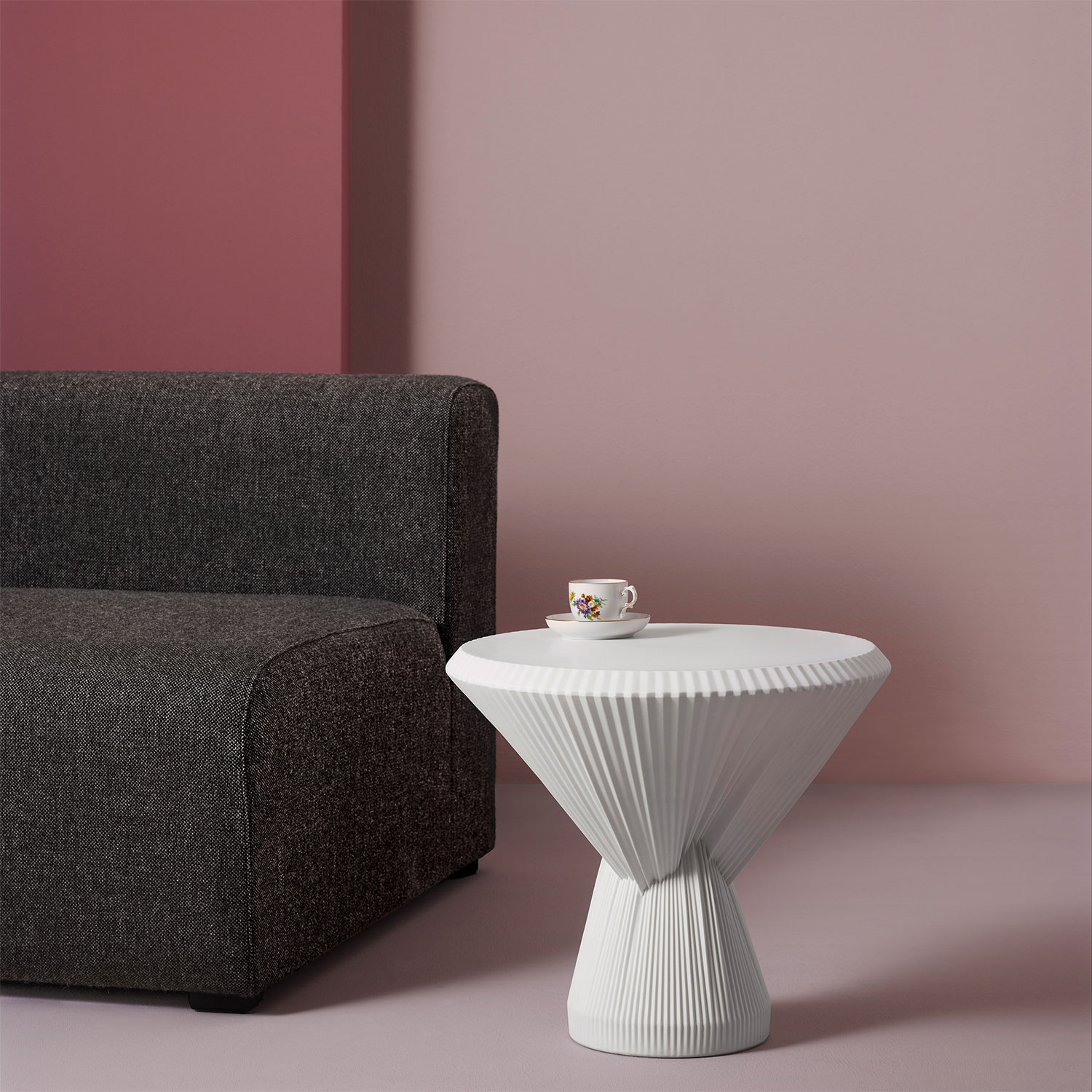 Weiße Kaffeetasse mit Blütenmotiv auf geriffeltem Tisch vor grauem Sofa. Fürstenberg Porzellan.