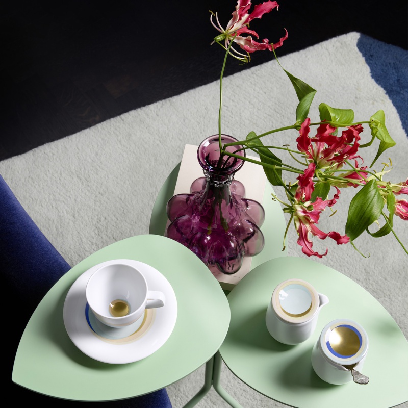 img3_FluenMotiv01089V4(1) Weiße Tasse und Vase mit Blumen auf grünem Tisch neben Sahnekännchen. Fürstenberg Porzellan.