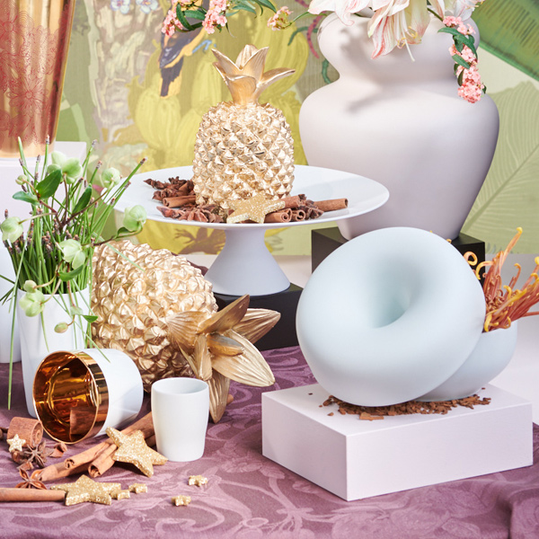 Goldene Ananas steht dekorativ auf weißem Kuchenständer, zwischen Porzellanvasen platziert. Fürstenberg Porzellan.