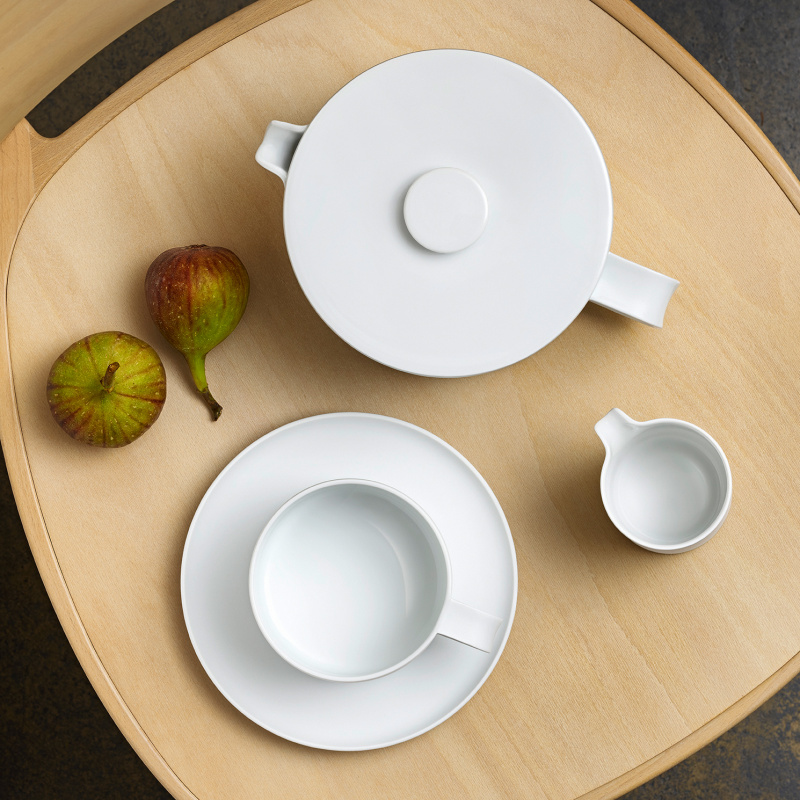 img2_tk20183_1001_teekanne Weiße Teekanne, Tasse und Milchkännchen auf Holztisch neben zwei Feigen. Fürstenberg Porzellan.