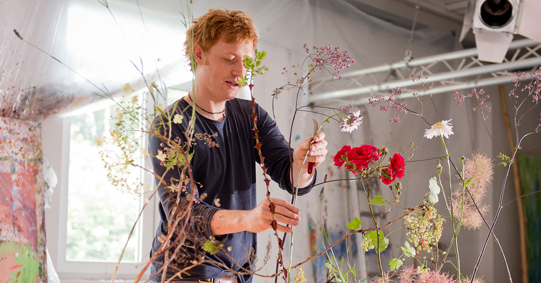 Mann arrangiert Blumensträuße in einem hellen Raum mit Fenster und Technik. Fürstenberg Porzellan.