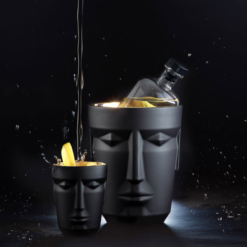 Schwarze Gefäße mit Gesichtsmotiven, ein Gefäß übergießt Flüssigkeit, Flasche im Eiskühler. Fürstenberg Porzellan.