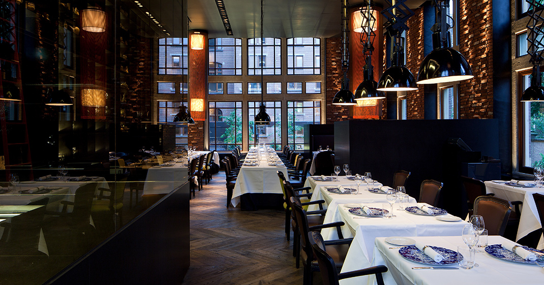 Schickes Restaurant mit gedeckten Tischen, eleganter Beleuchtung, großen Fenstern, industriellem Design. Fürstenberg Porzellan.