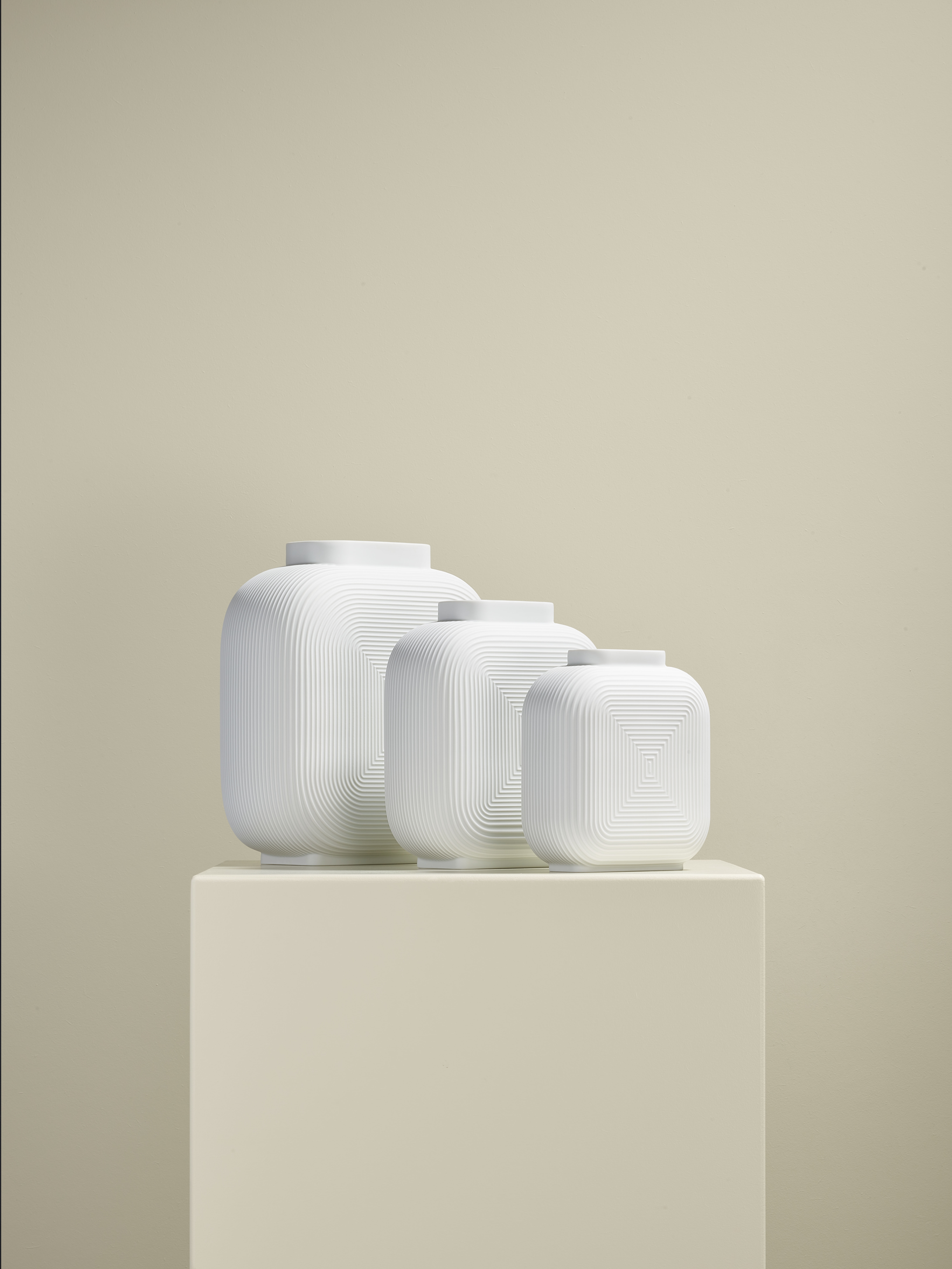 Drei weiße, strukturierte Vasen stehen auf einem hellen Podest. Fürstenberg Porzellan.