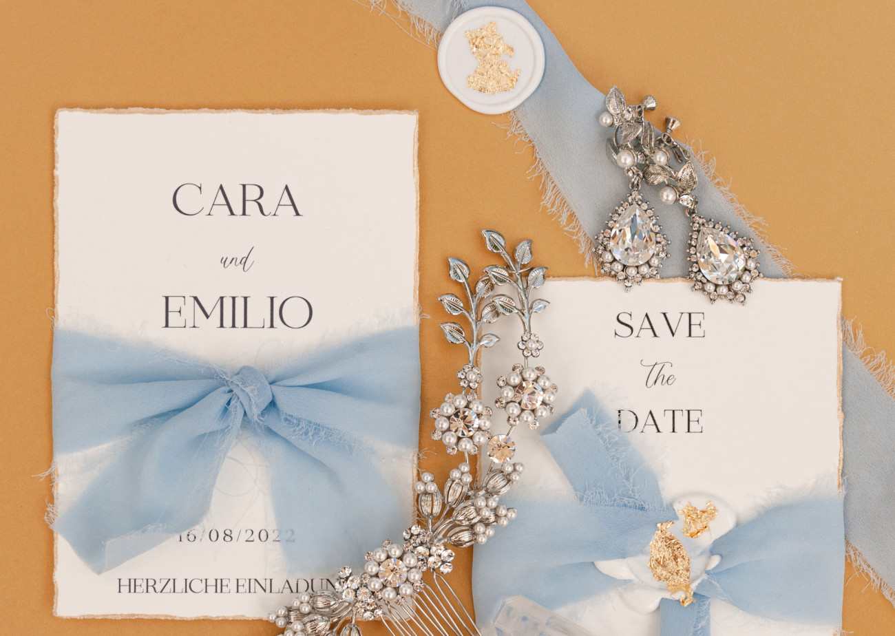 Einladungen aus Papier, beschriftet mit "CARA und EMILIO" und "SAVE the DATE". Fürstenberg Porzellan.