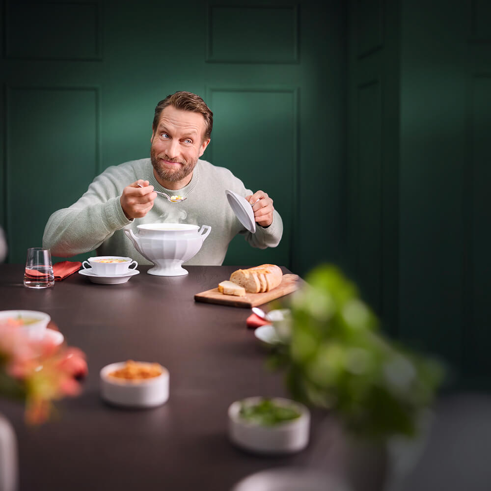 Weiße Porzellan-Suppenschale der FÜRSTENBERG Kollektion Grecque Weiß im Einsatz beim Servieren einer Suppe an einem stilvoll gedeckten Tisch.