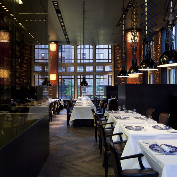 Gedeckte Tische stehen in elegantem Restaurant mit großen Fenstern, stilvoll beleuchtet. Fürstenberg Porzellan.