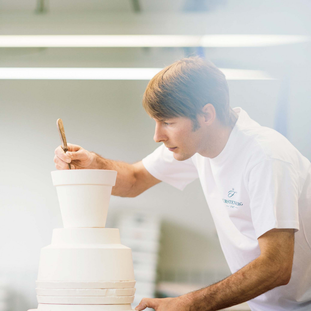 Mann bemalt Porzellantage, trägt weißes Fürstenberg-Porzellan-T-Shirt. Fürstenberg Porzellan.