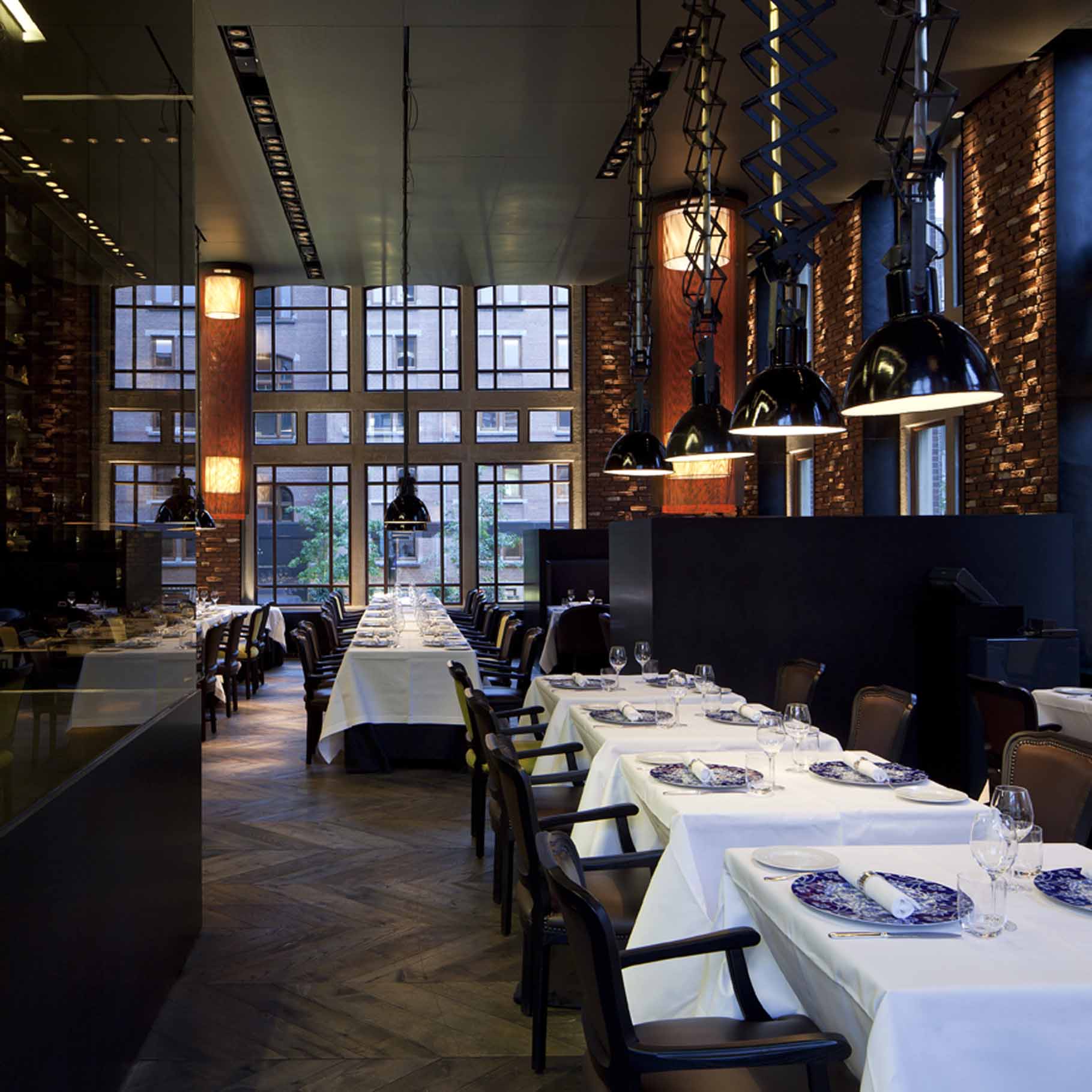 Elegantes Restaurant mit weißen Tischdecken und geometrischem Besteck, große Fenster, dunkle Hängelampen. Fürstenberg Porzellan.