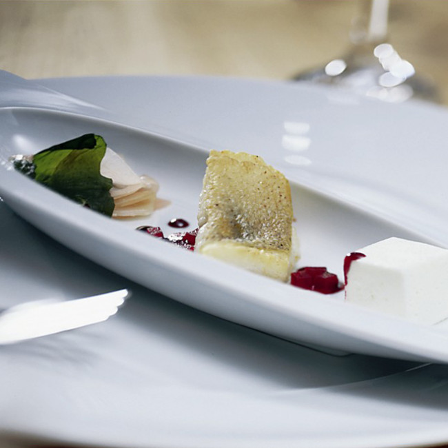 Fischfilet mit Beilage und Dessert kunstvoll auf weißem ovalem Teller präsentiert. Fürstenberg Porzellan.
