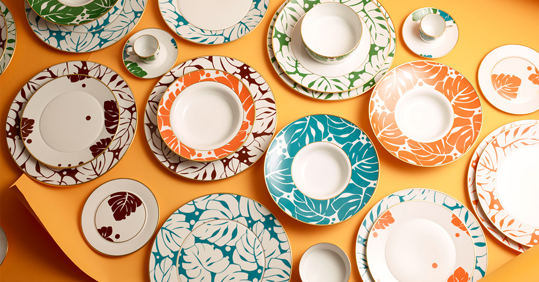 Bunte, floral gemusterte Porzellanteller auf orangefarbenem Hintergrund angeordnet. Fürstenberg Porzellan.