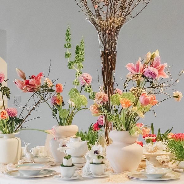 Vasen mit bunten Blumenarrangements auf gedecktem Tisch, umgeben von Geschirr. Fürstenberg Porzellan.