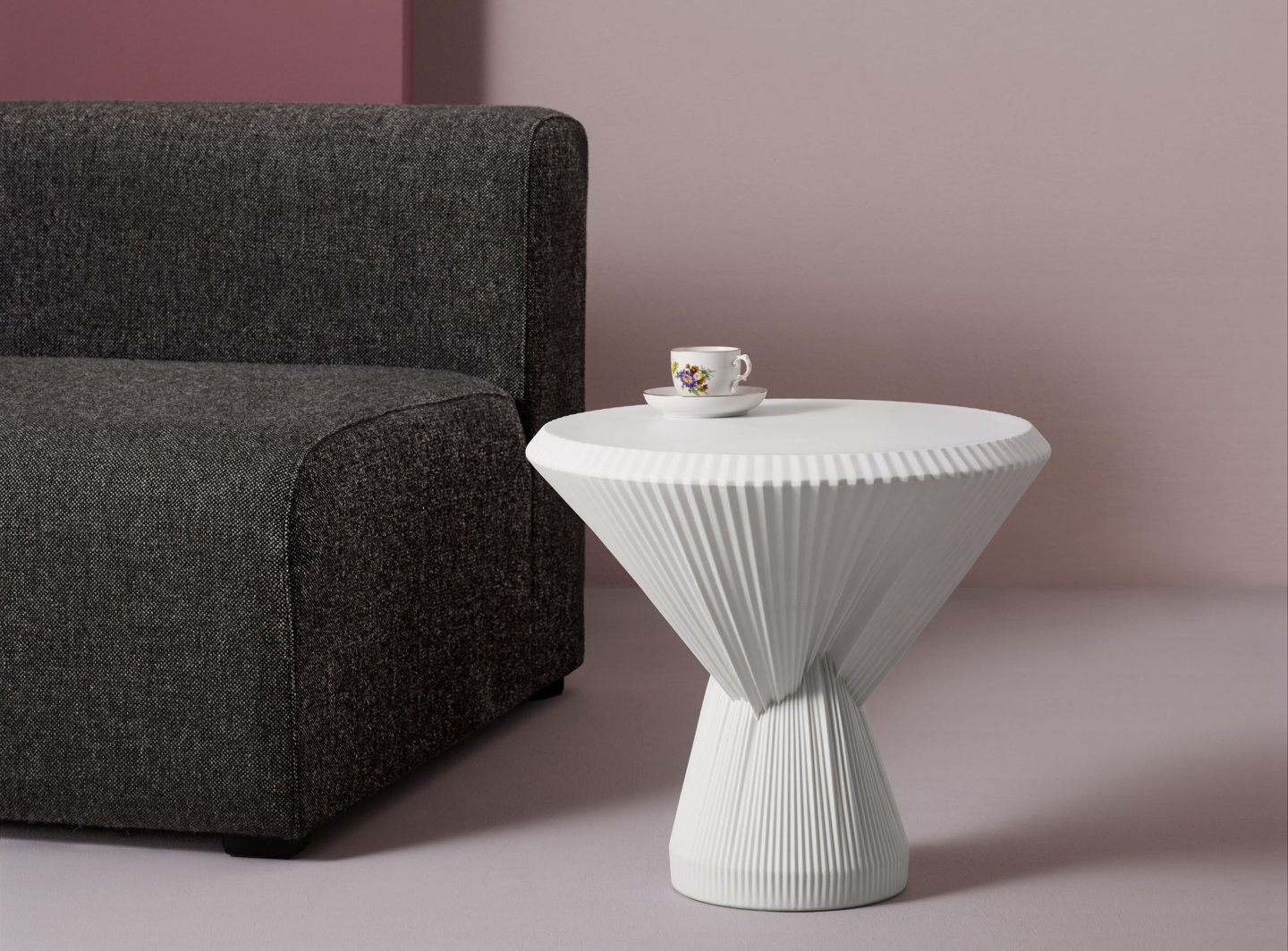 Weißer Tisch mit Tasse neben grauem Sofa vor rosa Wand. Fürstenberg Porzellan.
