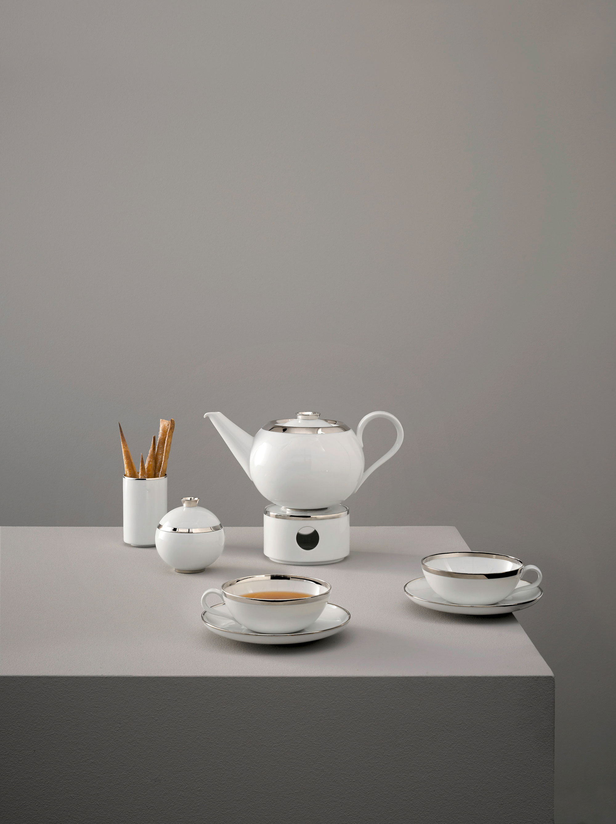 Weiße Teekanne, Tassen, Zuckerdose mit silbernen Rändern auf grauem Hintergrund. Fürstenberg Porzellan.