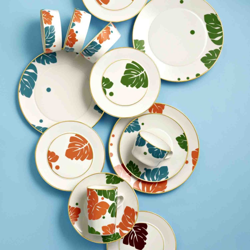 img2_un20145_70027_universaluntere Porzellangeschirr mit bunten Blättermotiven und Goldrand auf blauem Hintergrund angeordnet. Fürstenberg Porzellan.