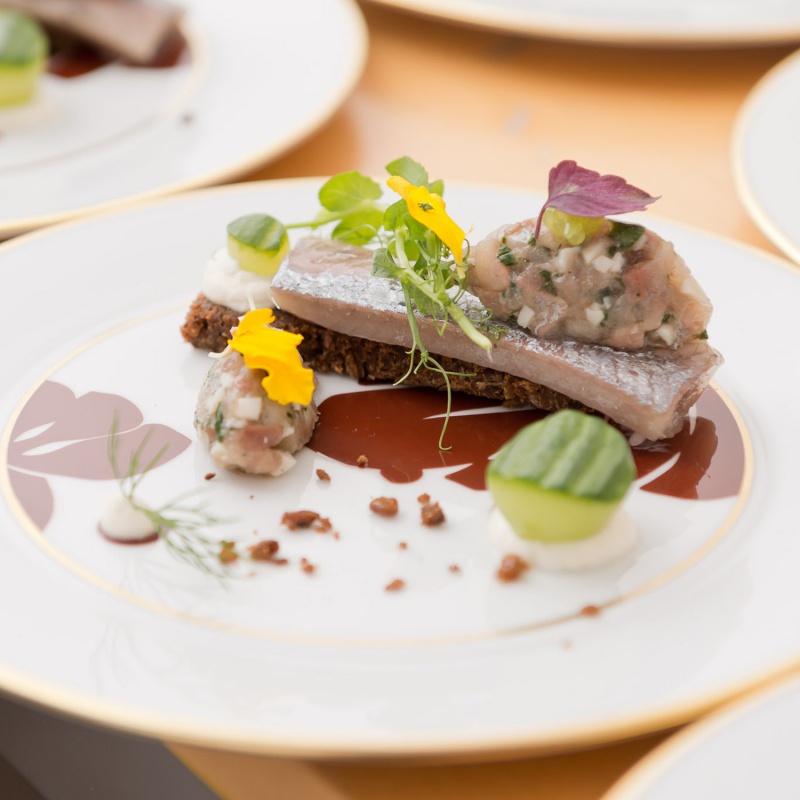 img3_ManuF-D-DSC6900(1) Fein angerichteter Fisch mit Kräutern und essbaren Blüten auf Porzellanteller. Fürstenberg Porzellan.