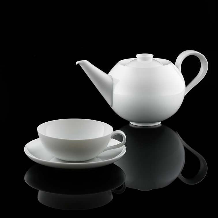 Weiße Porzellankanne und Tasse mit Untertasse spiegeln sich auf schwarzer Oberfläche. Fürstenberg Porzellan.