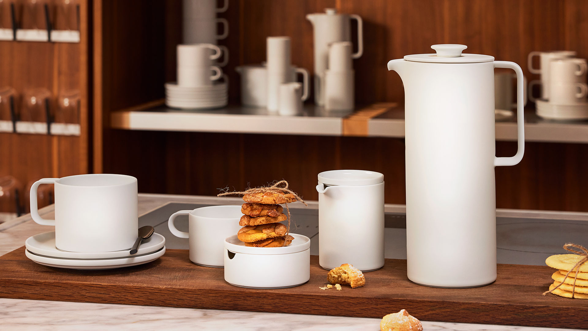 Weiße Geschirrkollektion mit Tasse, Kanne, Bechern, Keksen auf Holzbrett, Küche. Fürstenberg Porzellan.
