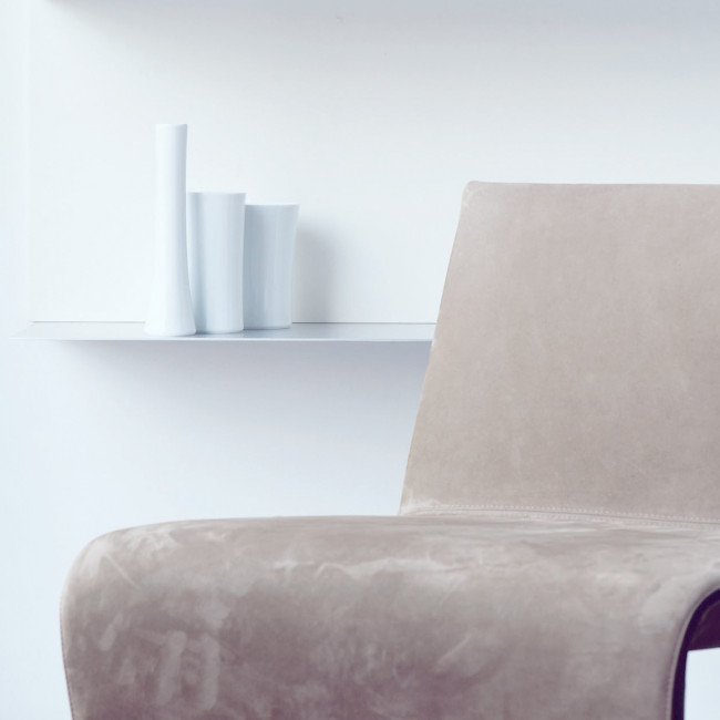 Beige Stuhl neben einem Regal mit weißen Vasen im minimalistischen Raum. Fürstenberg Porzellan.