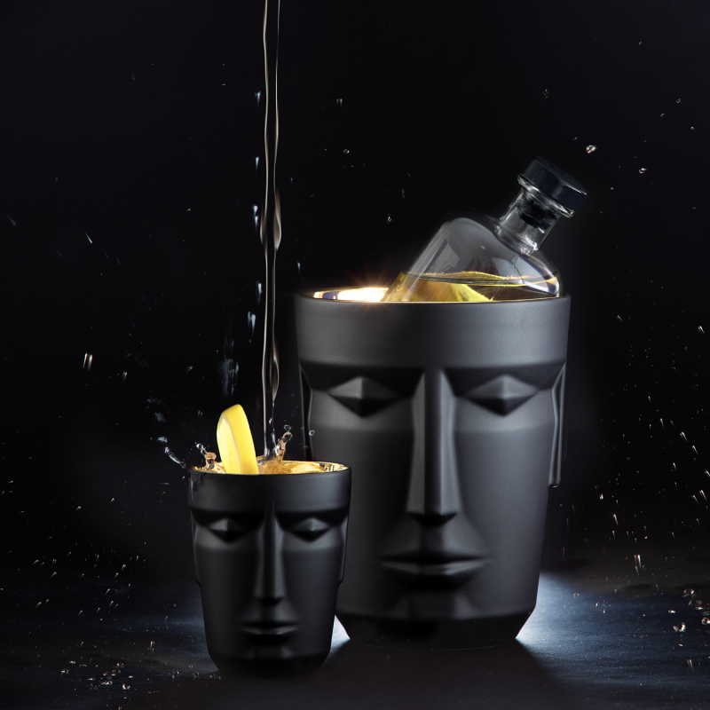 img3_bk1882206103_ice_bucket_prometheus__mattsatiniert__schwarz Mattschwarze Gesichtvase mit Flasche, daneben Gesichtbecher mit Zitronenscheibe; Flüssigkeit spritzt. Fürstenberg Porzellan.