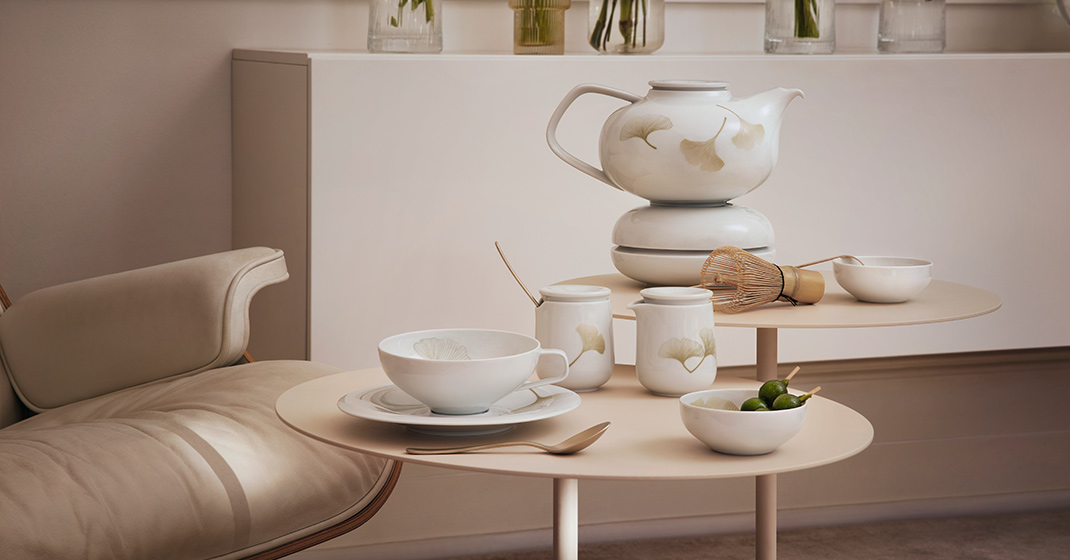 Teeservice mit Ginkgo-Muster auf Tisch, daneben Rührbesen und kleine Schalen. Fürstenberg Porzellan.