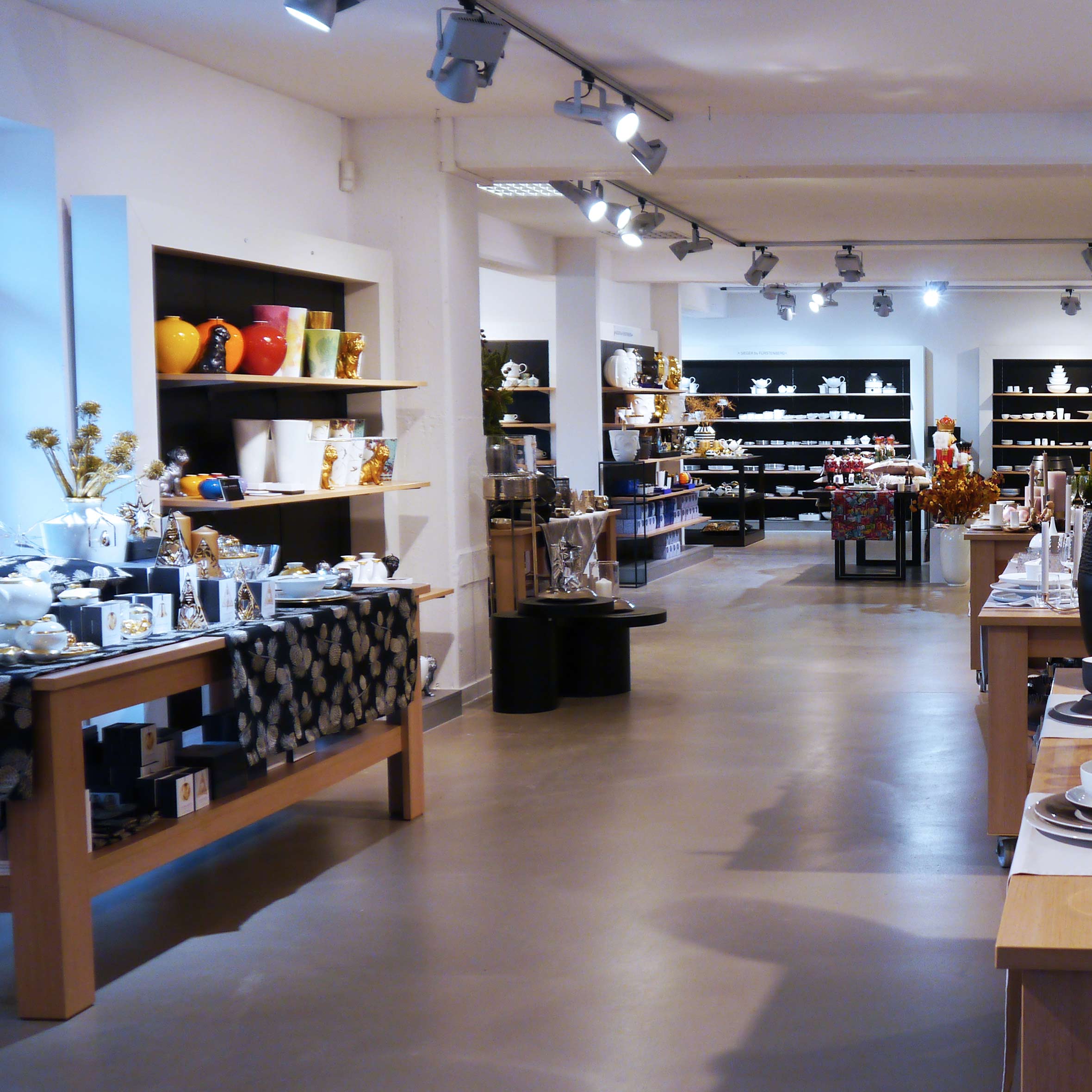 Showroom zeigt Porzellanartikel auf Holzregalen, beleuchtet durch Deckenspots. Fürstenberg Porzellan.