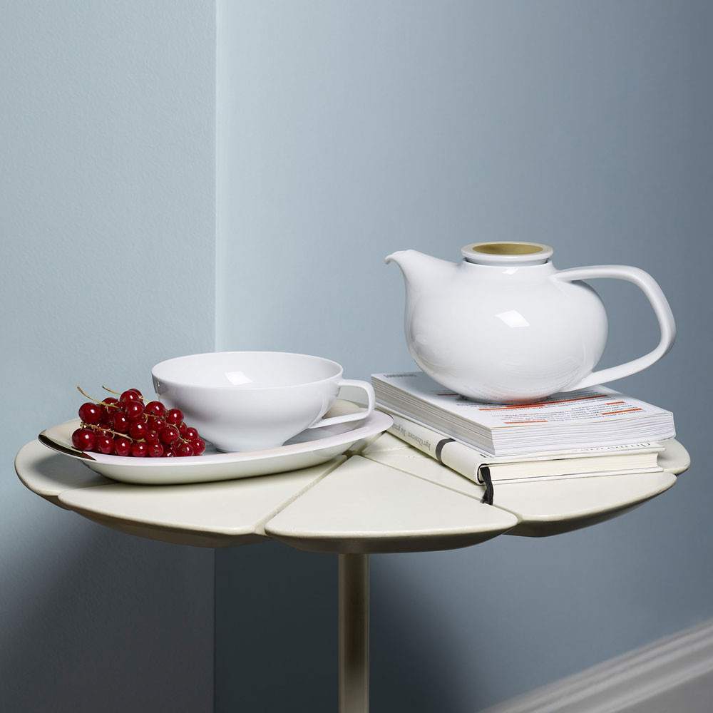 Weiße Teekanne und Tasse auf Tisch, ein Teller mit roten Johannisbeeren. Fürstenberg Porzellan.