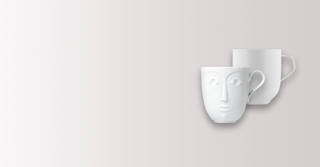 Zwei weiße Tassen mit Gesichtsmotiven vor neutralem Hintergrund. Fürstenberg Porzellan.