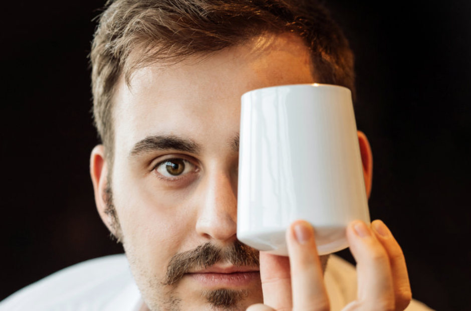 Weiße Tasse verdeckt teilweise Gesicht eines Mannes. Fürstenberg Porzellan.
