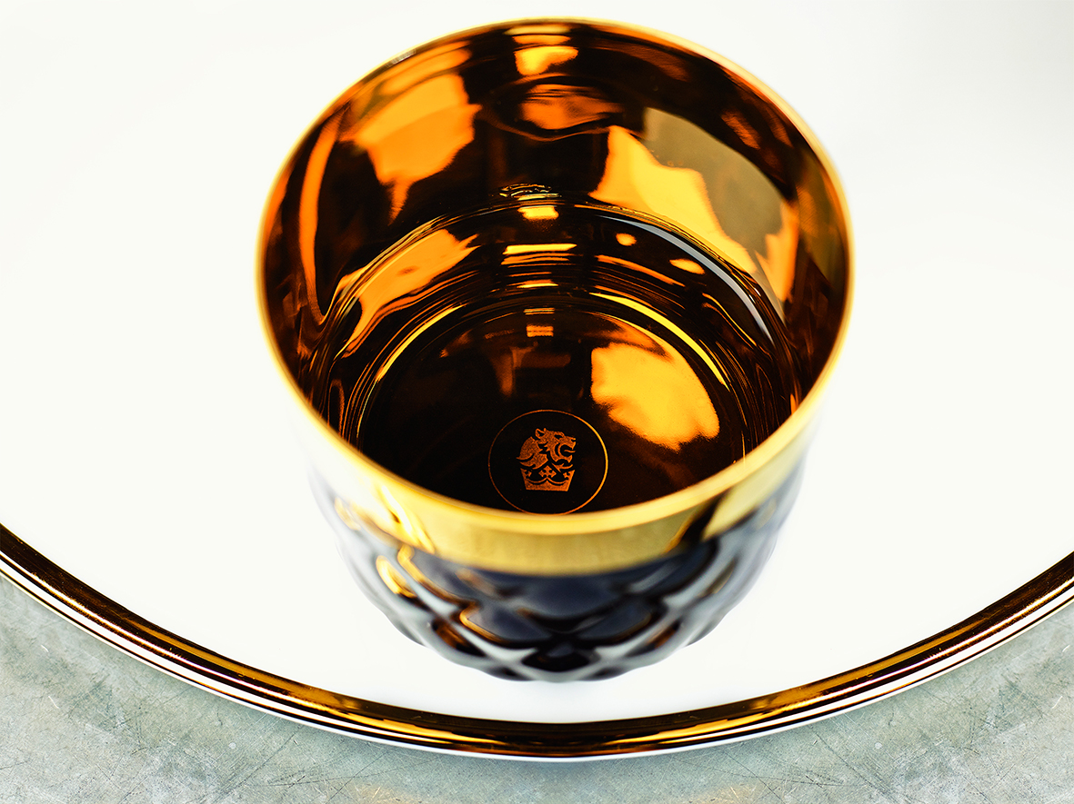 Goldene, glänzende Porzellantasse mit dekorativem Muster, steht auf passendem Teller. Fürstenberg Porzellan.