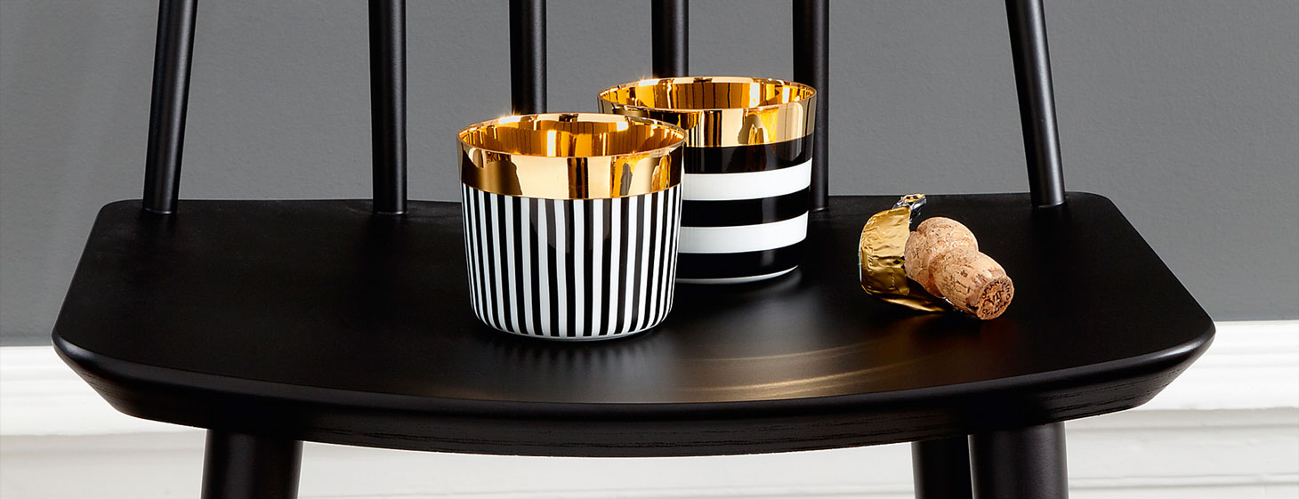 Zwei goldene Becher mit schwarz-weißen Streifen stehen auf schwarzem Stuhl. Fürstenberg Porzellan.