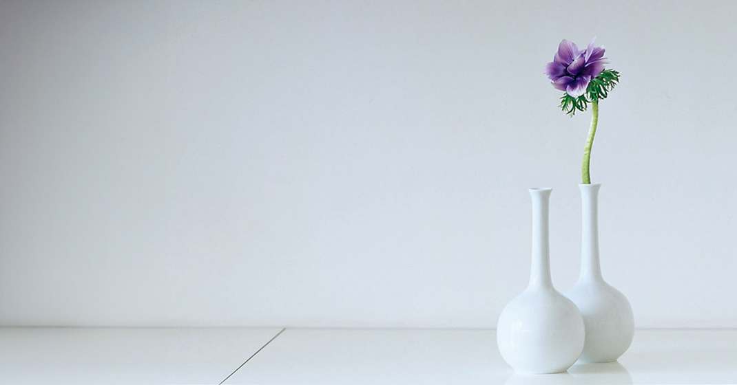 Zwei weiße Vasen, eine mit violetter Blume, stehen auf weißem Tisch. Fürstenberg Porzellan.