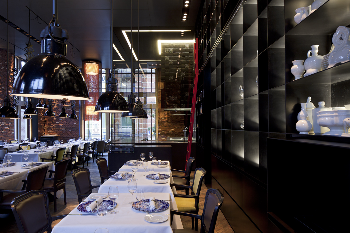 Restaurant mit gedeckten Tischen, großen schwarzen Lampen, und dekorativem Porzellan an der Wand. Fürstenberg Porzellan.
