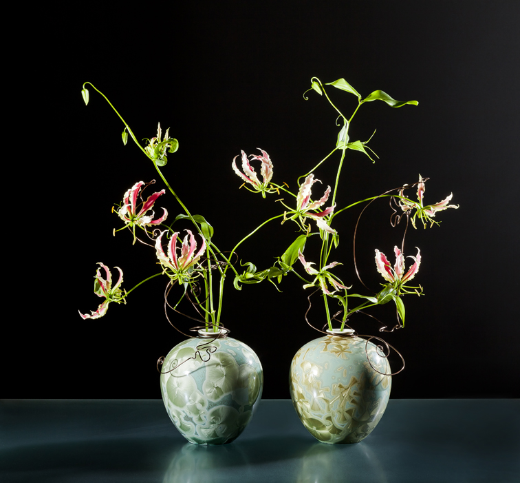 Zwei Porzellanvasen mit floralen Mustern, halten verzweigte Lilienblüten auf schwarzem Hintergrund. Fürstenberg Porzellan.